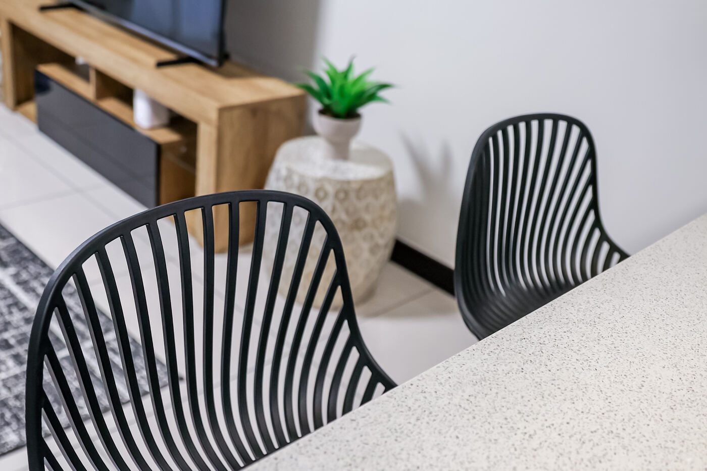 Open-plan lounge and dining area with black slatted chairs and a leafy plant