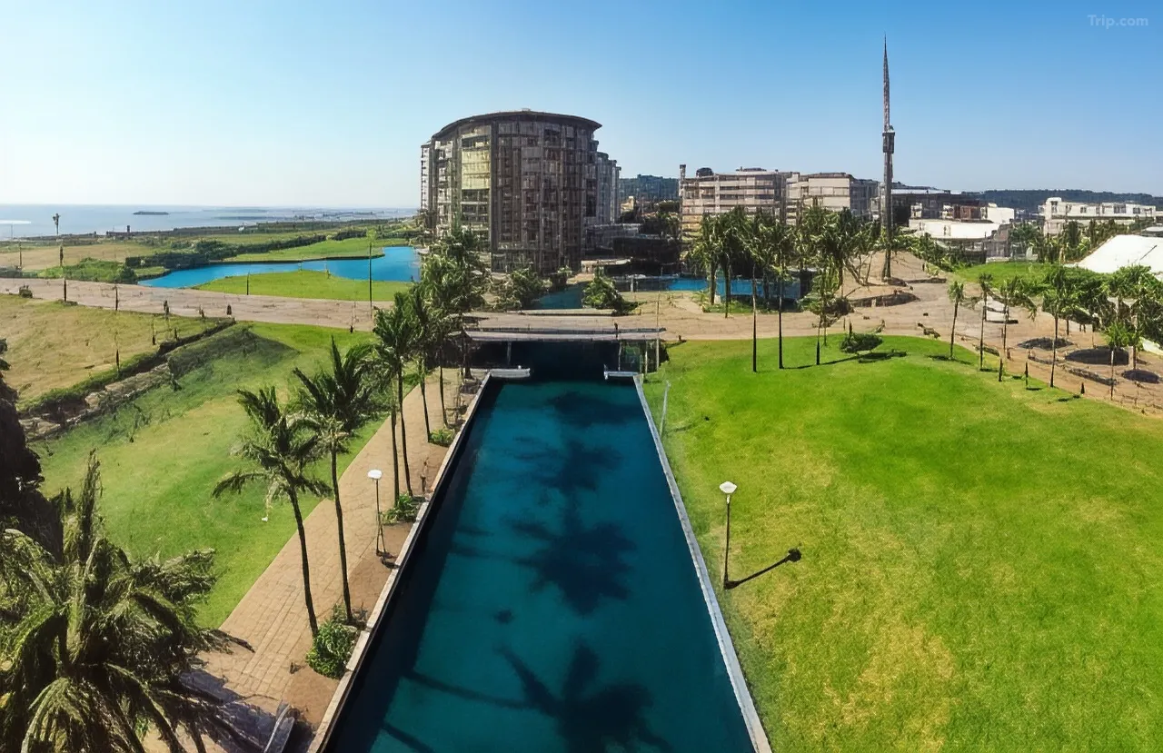 Aerial view of a palm-lined canal and green lawns at the Durban Point Waterfront, with a curved apartment building and the Indian Ocean in the distance