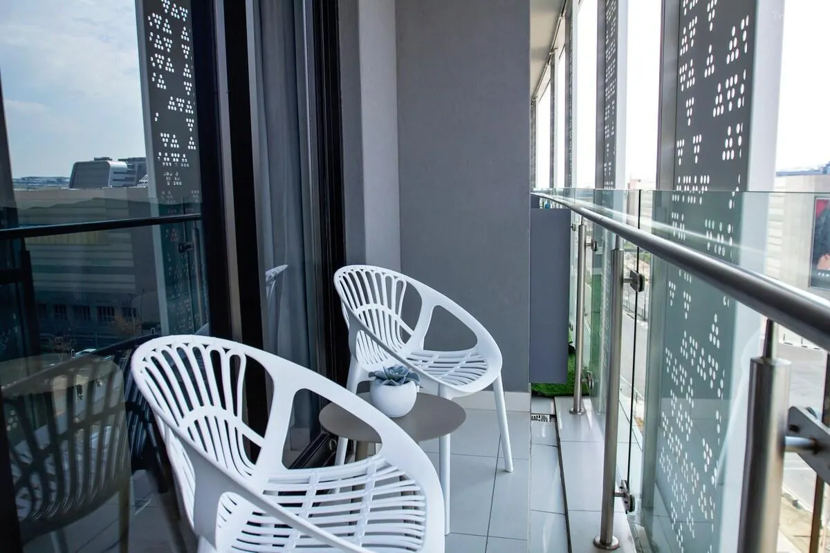 Private balcony with two white woven tub chairs and a small round table holding a succulent, framed by a glass balustrade and decorative screens overlooking Waterfall City
