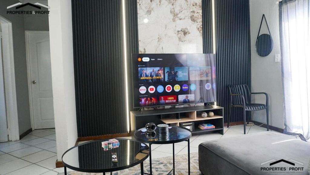 Lounge with a large smart TV on a black slatted feature wall, glass nesting coffee tables and a soft grey couch